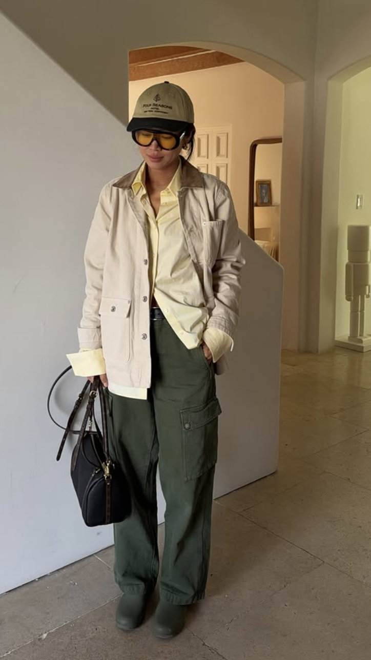 A person wearing oversized olive green wide-leg cargo pants with a cream button-down shirt, a black leather belt, and carrying a black top-handle handbag