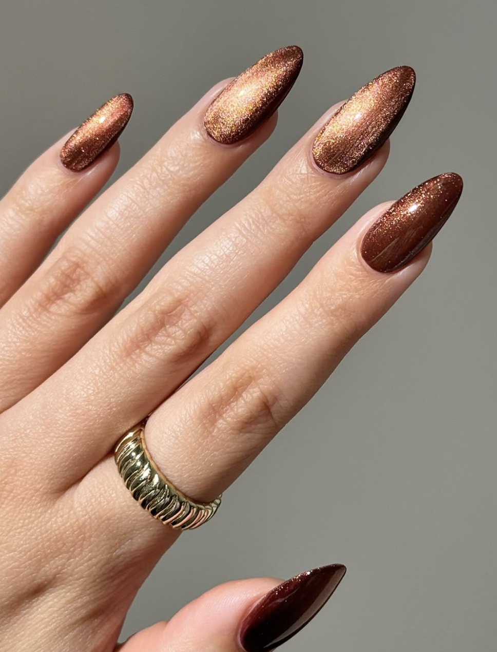Long, almond-shaped nails showcasing a warm, shimmering maple bronze chrome finish that catches the light with a metallic golden glow.