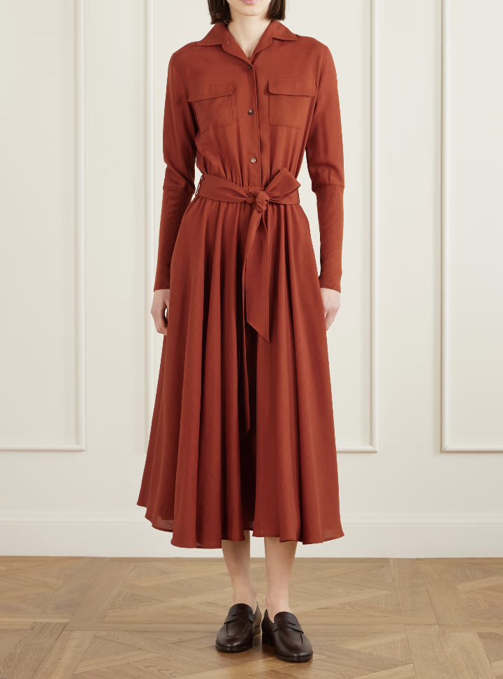 A woman wearing a rust-colored Loro Piana Verlaine belted pleated wool midi shirt dress, representing old money style and luxury craftsmanship.