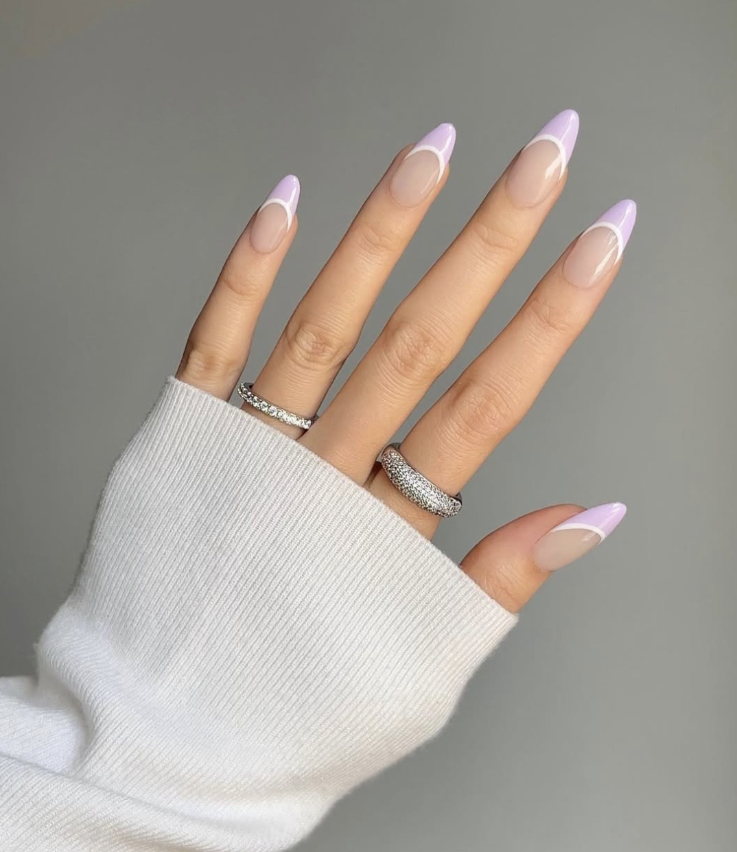 Almond-shaped nails with a sheer nude base and a soft, pale lavender purple French tip.