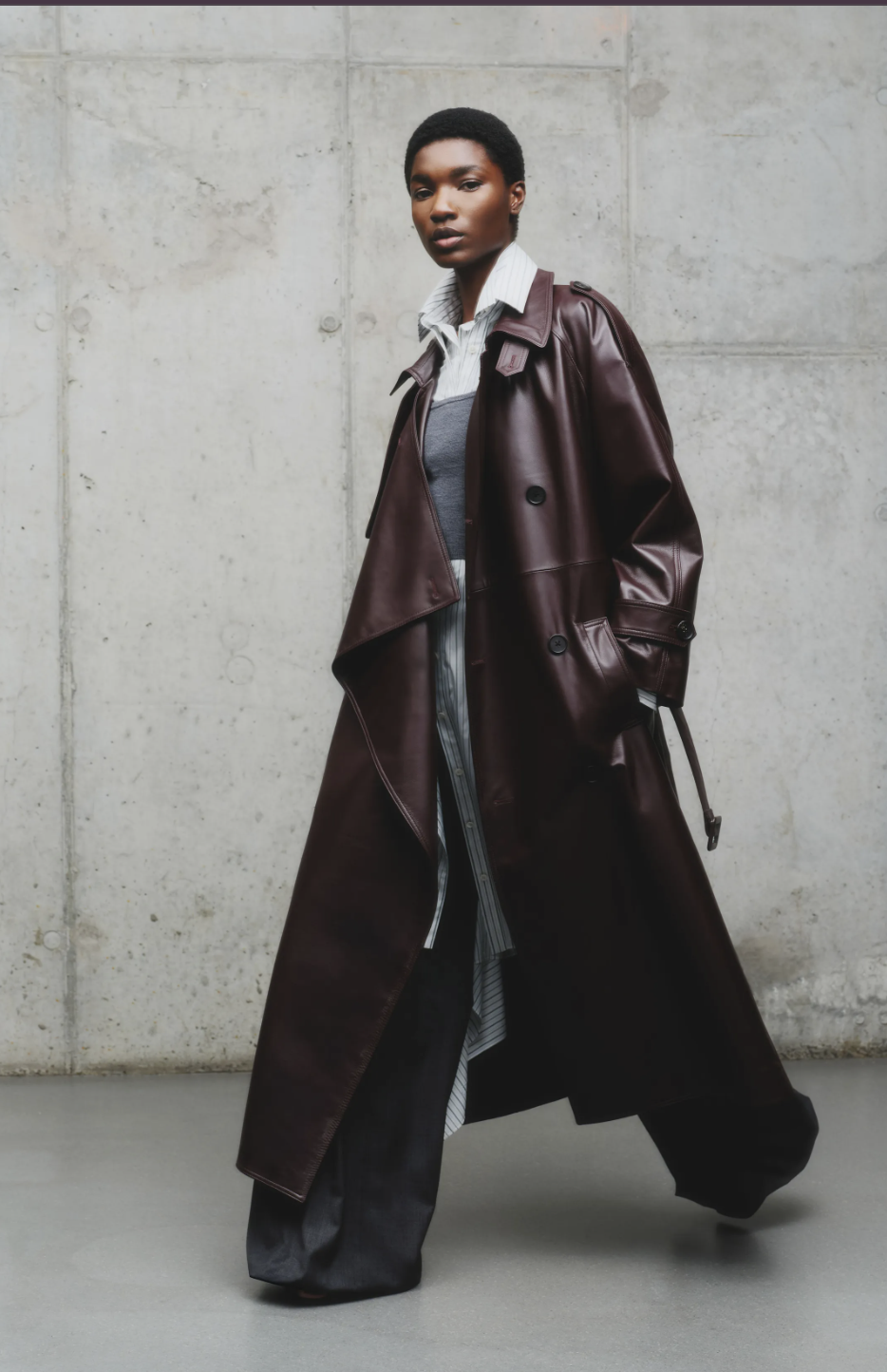 A model on the Monse Fall/Winter 2026 runway wearing a belted, floor-length aubergine leather trench coat, highlighting the deep purple power neutral trend.