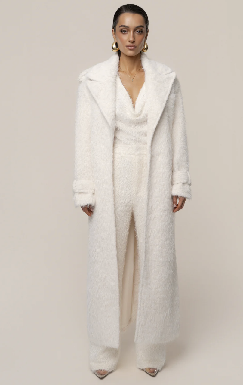 Woman wearing a long ivory wool oversized coat over matching cream wide-leg trousers and silver pointed-toe heels.