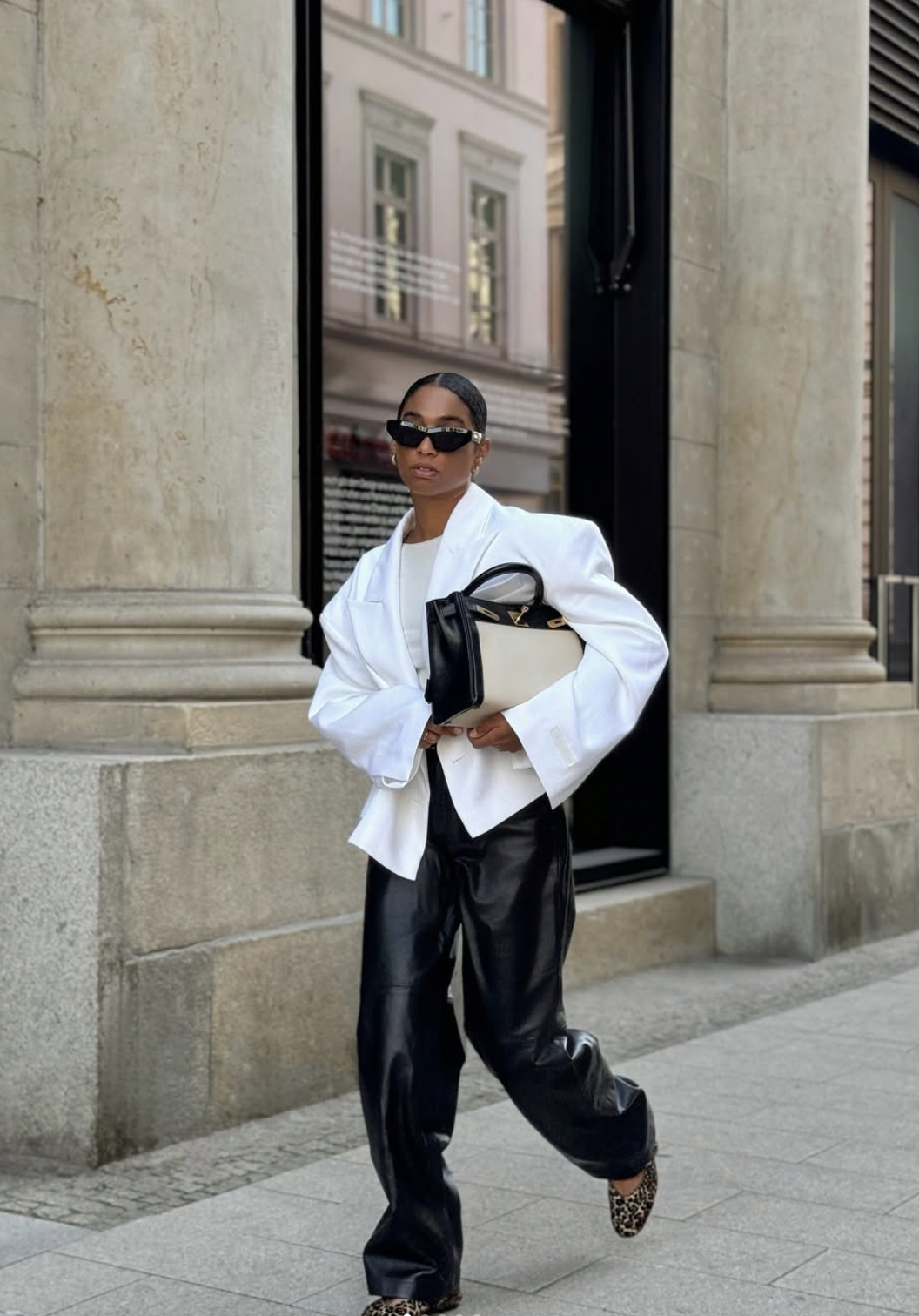 Woman wearing black wide-leg leather pants, an oversized white button-down shirt and leopard print flats
