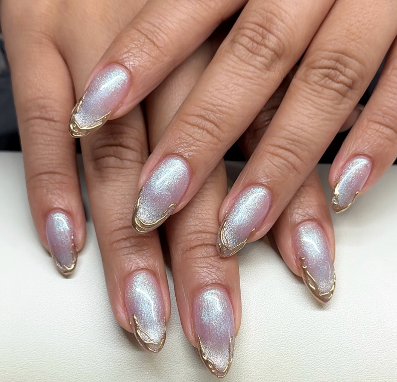 Long almond-shaped nails with a sheer iridescent chrome finish that glows blue and purple, featuring a delicate 3D metallic gold rim along the edges.