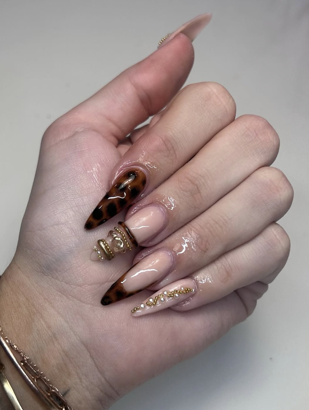 Pointed almond nails with tortoise shell patterns, nude bases, and elaborate 3D gold bands with pearl and gemstone clusters.