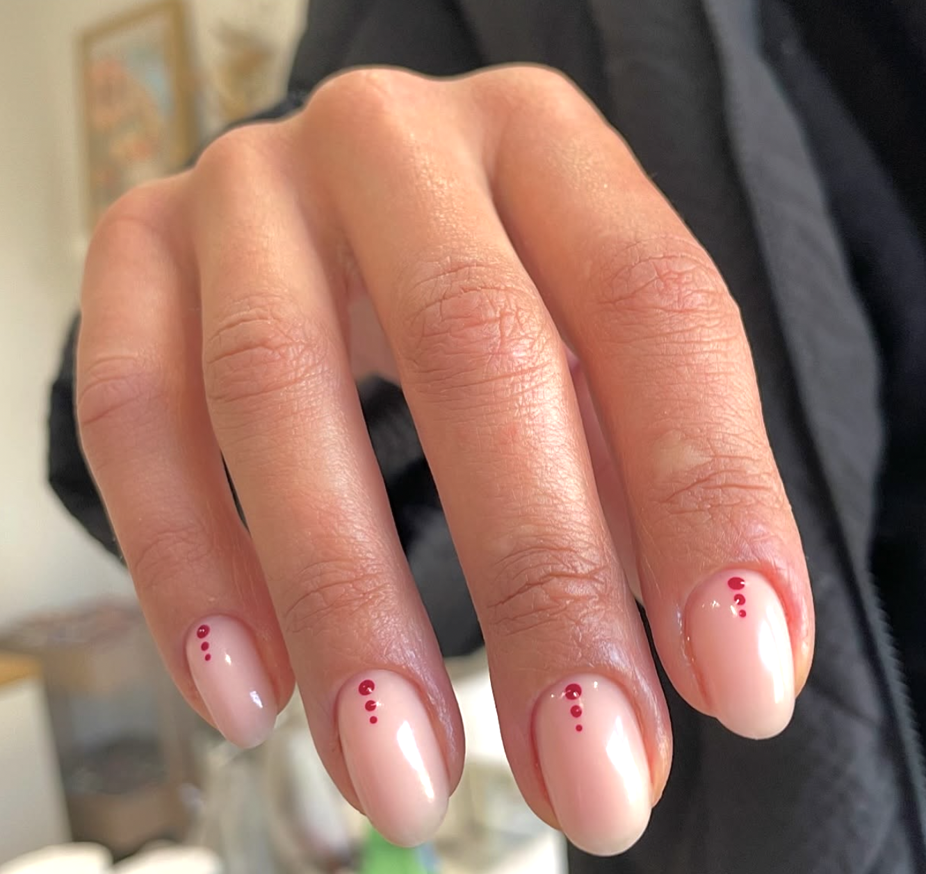 Medium almond-shaped nails with a glossy nude base, featuring a neat row of tiny cherry red micro-dots aligned vertically down the center of each nail.