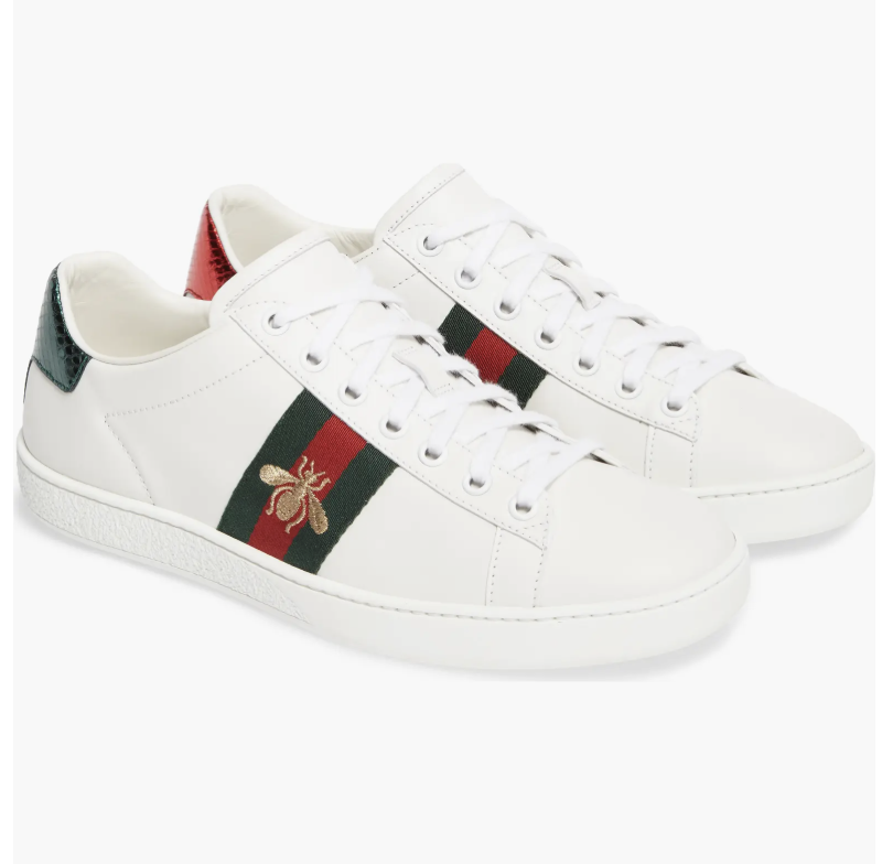 A pair of white leather Gucci New Ace sneakers with signature green and red stripes, styled as luxury work sneakers for a professional office environment.