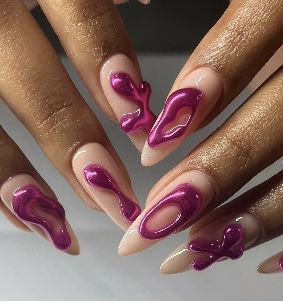 A close-up of long, tapered nails with 3D molten pink chrome accents on a sheer neutral base.
