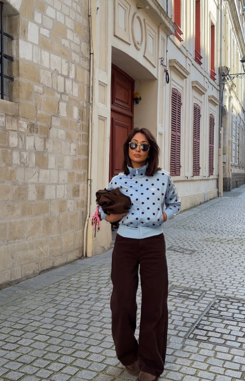 A woman sitting on stone steps wearing wide-leg white pants with a black polka dot print, paired with an oversized baby blue half-zip ribbed knit sweater and metallic silver sneakers.