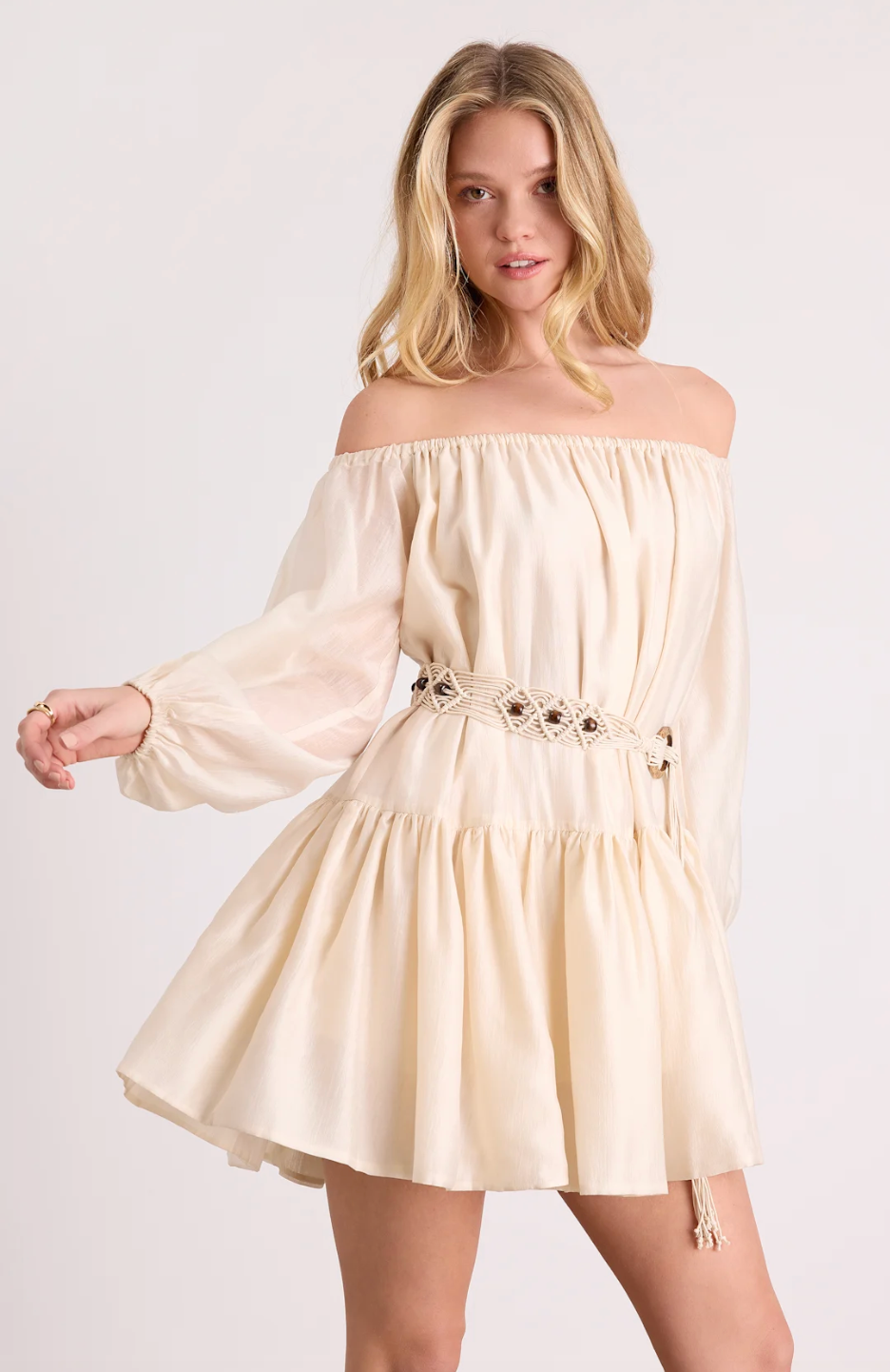 Front view of a blonde woman modeling a cream-colored, off-the-shoulder mini dress with long billowy sleeves, a smocked elastic neckline, and a flirty tiered skirt.