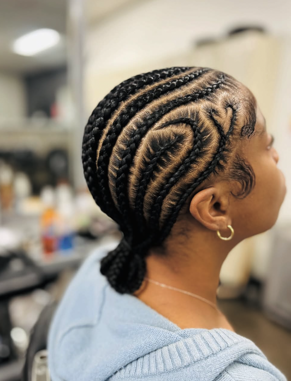 Close-up view of a woman from behind showcasing a neat slick back cornrow bun hairstyle with a braided spiral design at the back of the head.