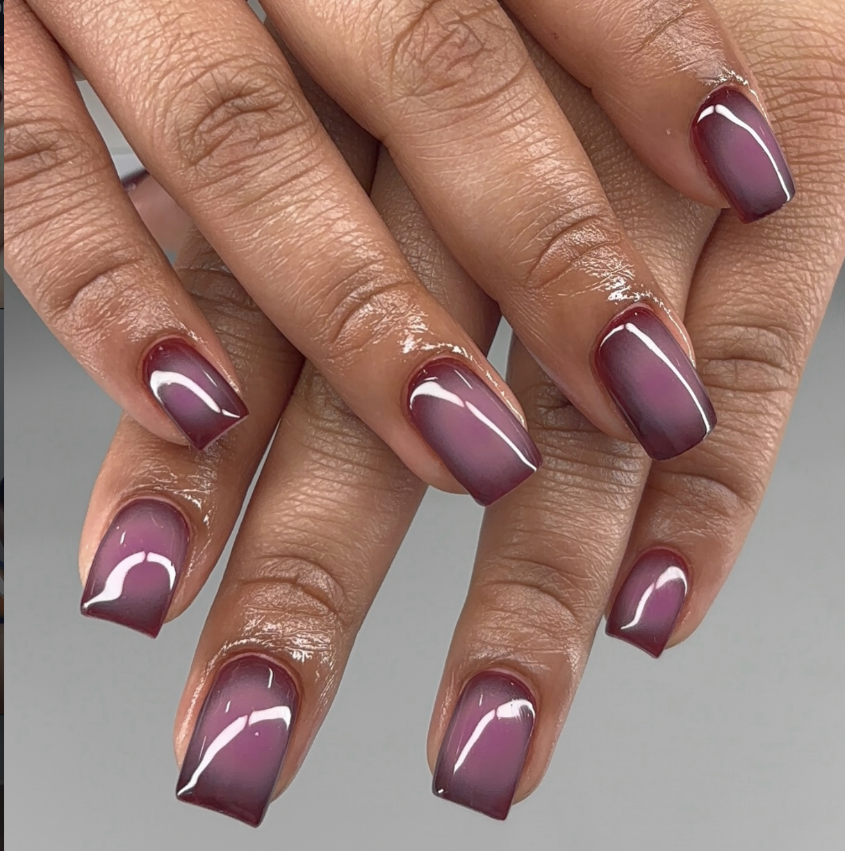 A close-up of short nails featuring a glossy purple mini aura nail design with a diffused center glow over a natural base.