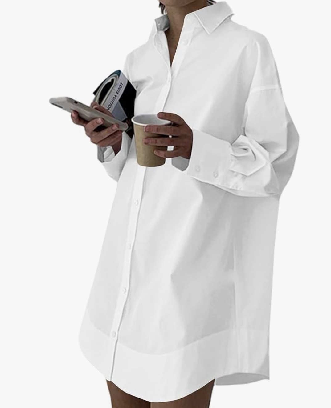 A person wearing an oversized white cotton poplin shirt dress from The Frankie Shop, holding a coffee cup and a magazine for a street-style look.