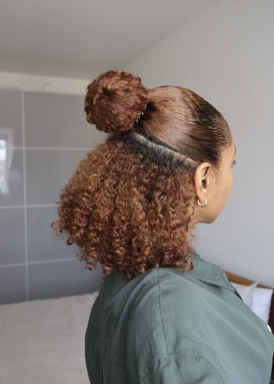 Side view of a woman showcasing a half-up, half-down protective hairstyle on rich auburn curly textured hair with a neat bun at the crown.