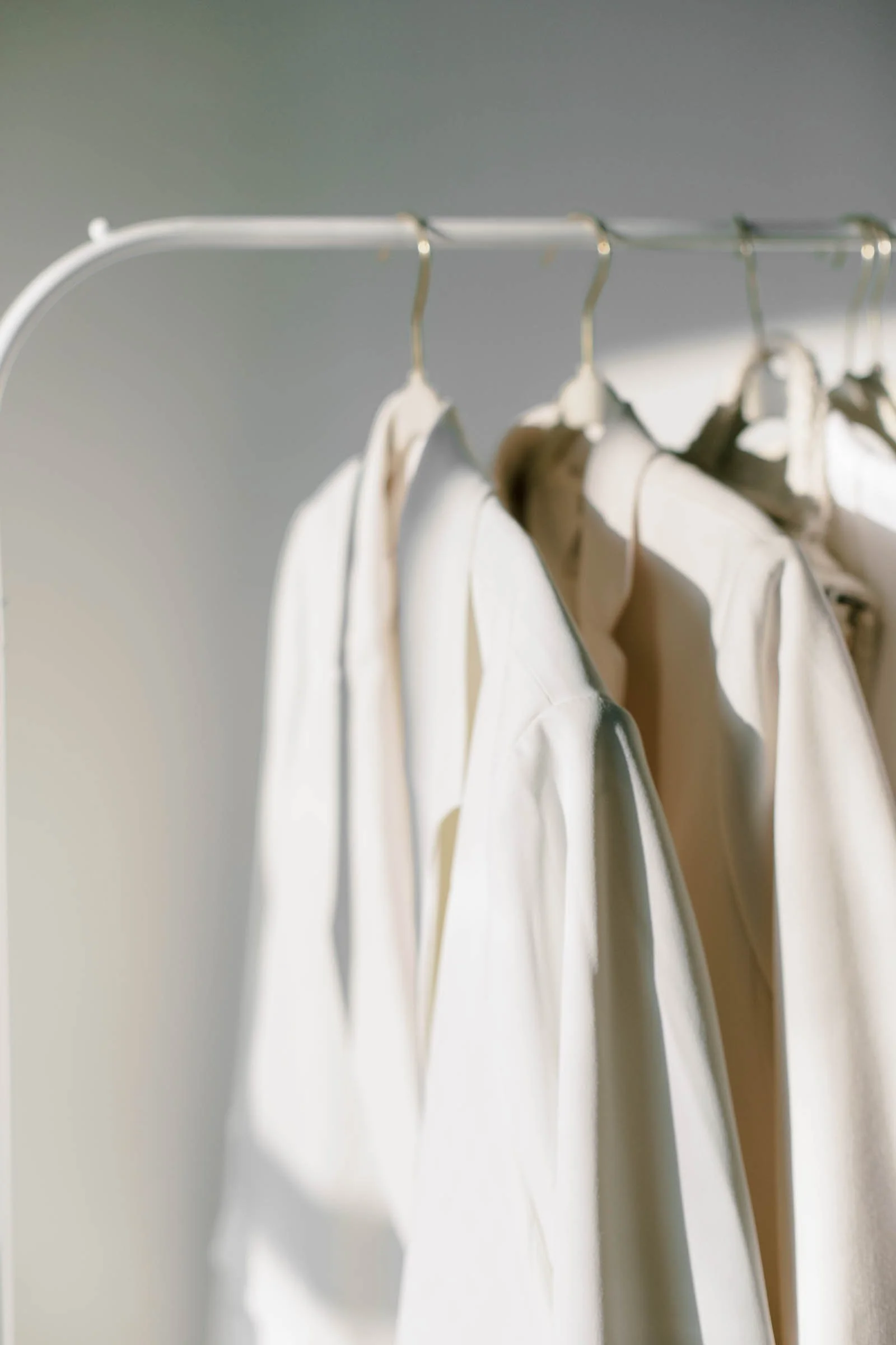 A close-up of cream-colored dresses hanging on a white clothing rack.