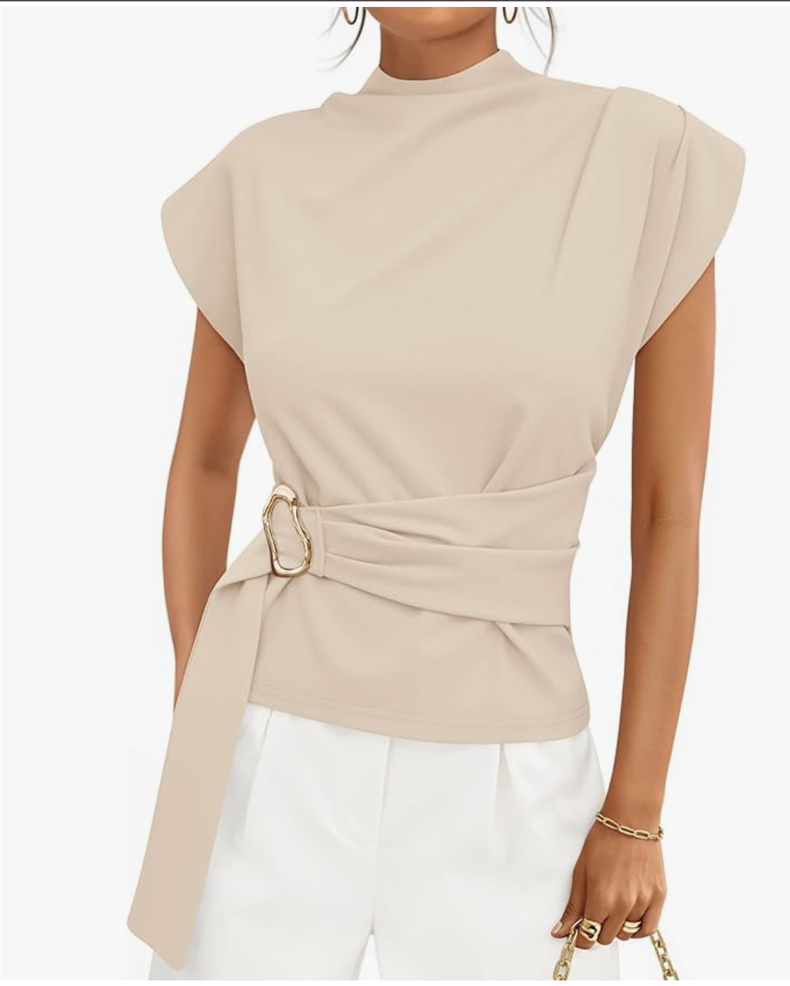 A woman wearing a beige draped wrap-style blouse with cap sleeves and a gold side buckle, styled with white trousers for a polished spring look for women in their 60s
