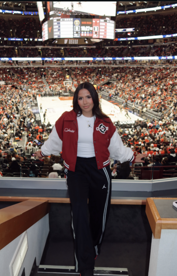 Woman wearing a red-and-white varsity jacket with a white top, black trousers and dark sunglasses.