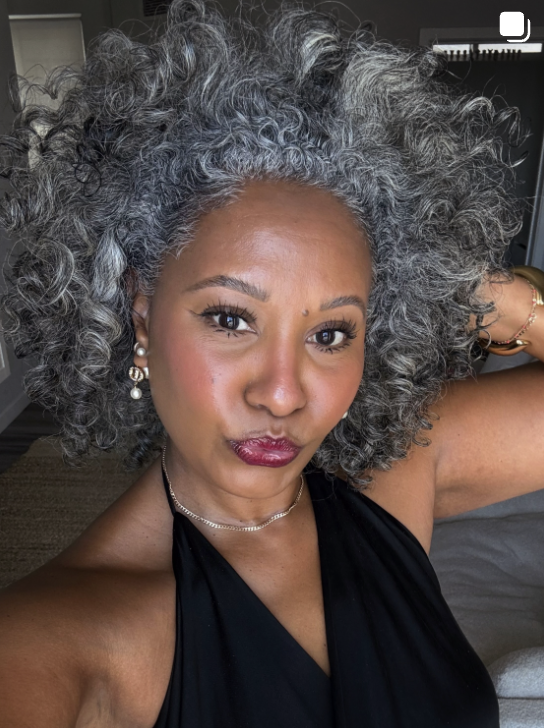 Woman wearing a full rounded crop of natural gray curls that frames her square face.