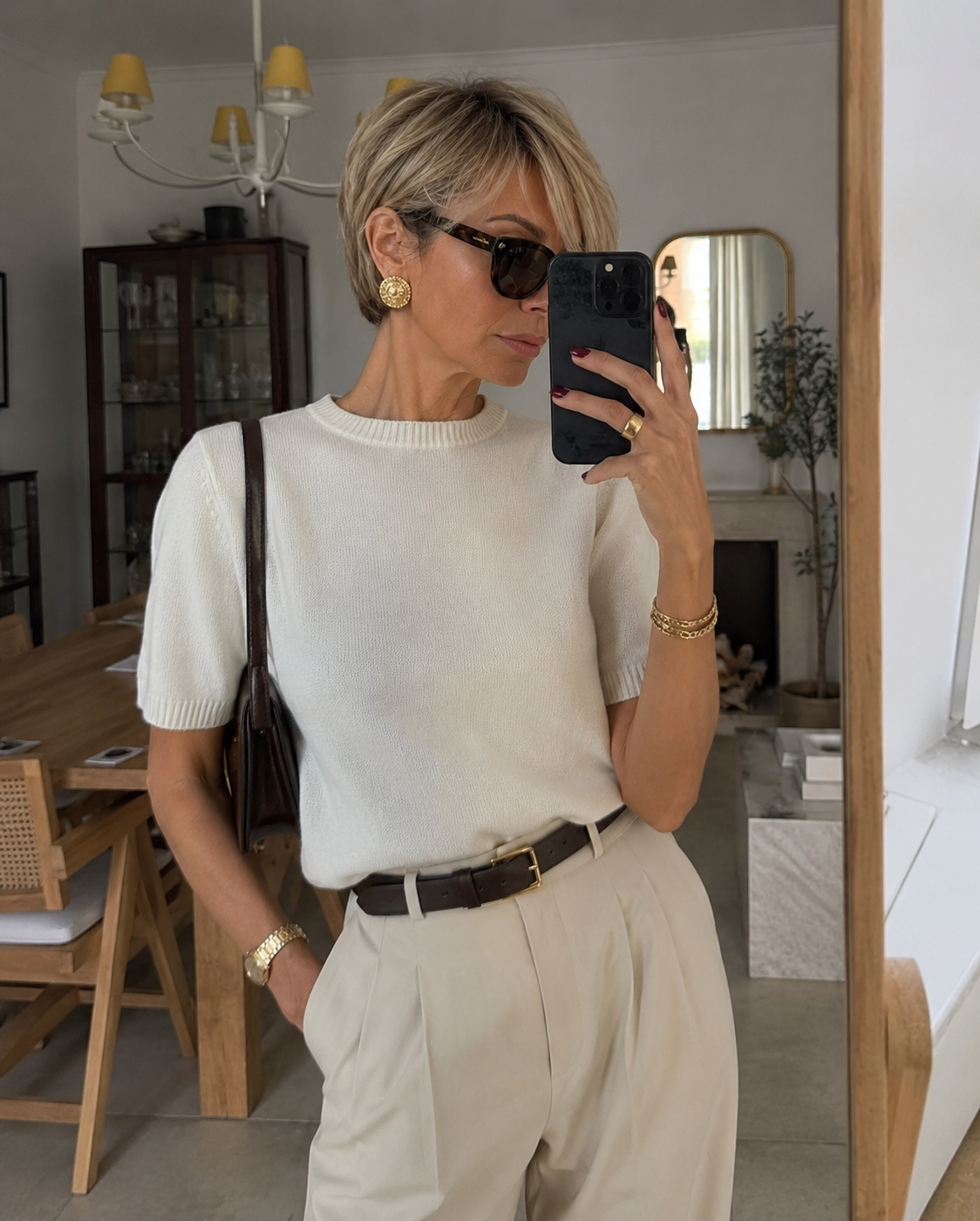 A chic woman over 50 with a modern blonde bixie haircut, featuring disconnected, textured layers, wearing a white short-sleeve top and sunglasses.