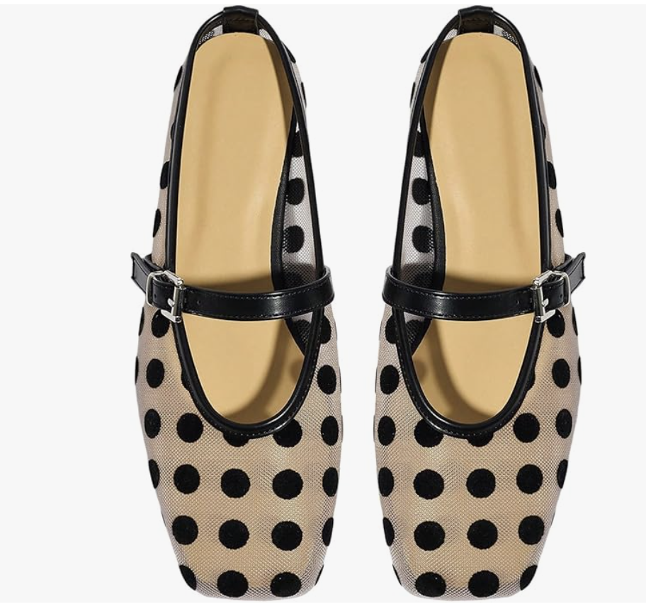 A close-up view of a pair of modern beige Mary Jane flats featuring a black polka-dot pattern, a square toe, and a thin black leather strap with a silver buckle.
