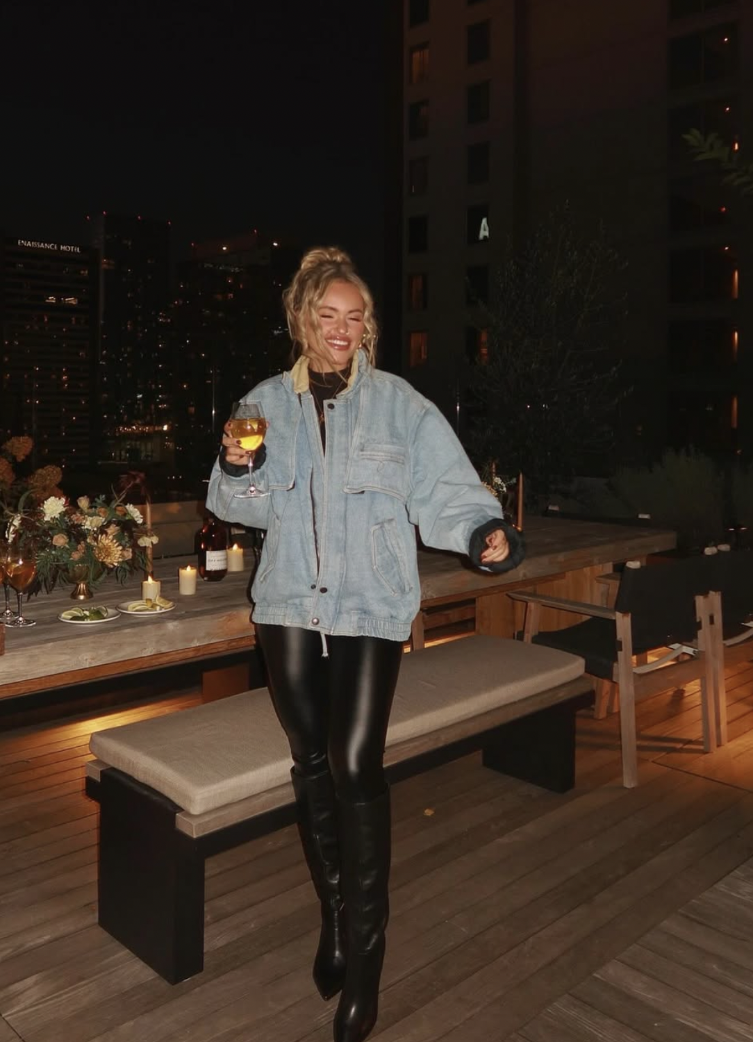 Woman wearing shiny black leather pants, an oversized denim jacket and black knee-high boots at an evening dinner party