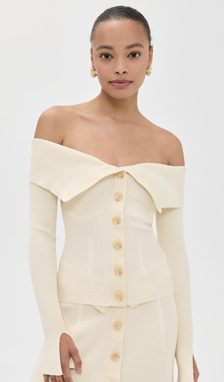 A woman wearing a cream-colored Zimmermann Rebellion Bandeau Cardigan, an off-the-shoulder button-up knit top.