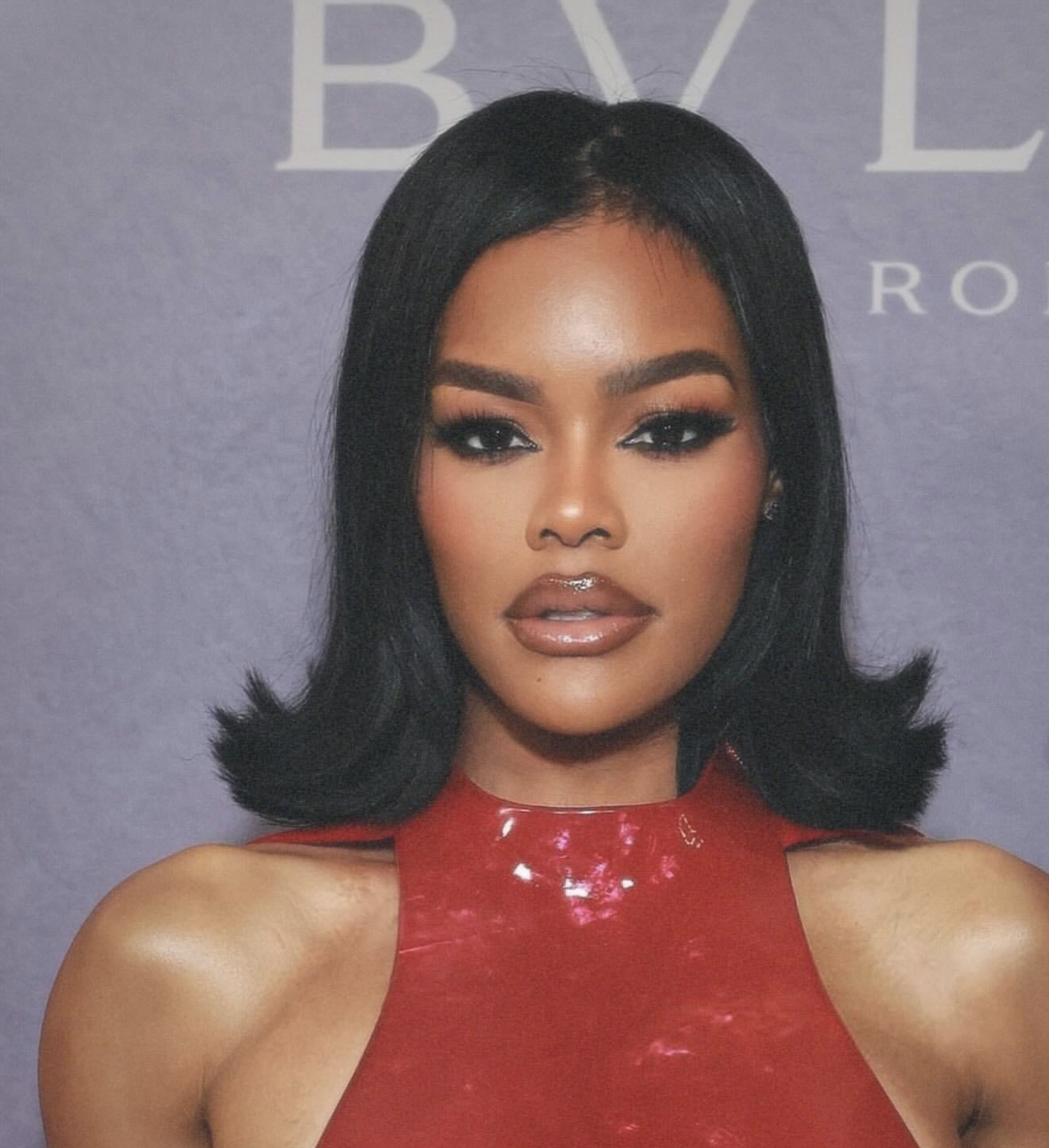 Teyana Taylor featuring a sleek, chin-length flipped bob with a side part, wearing a red high-neck top and showcasing sharp cheekbones characteristic of a diamond face shape.