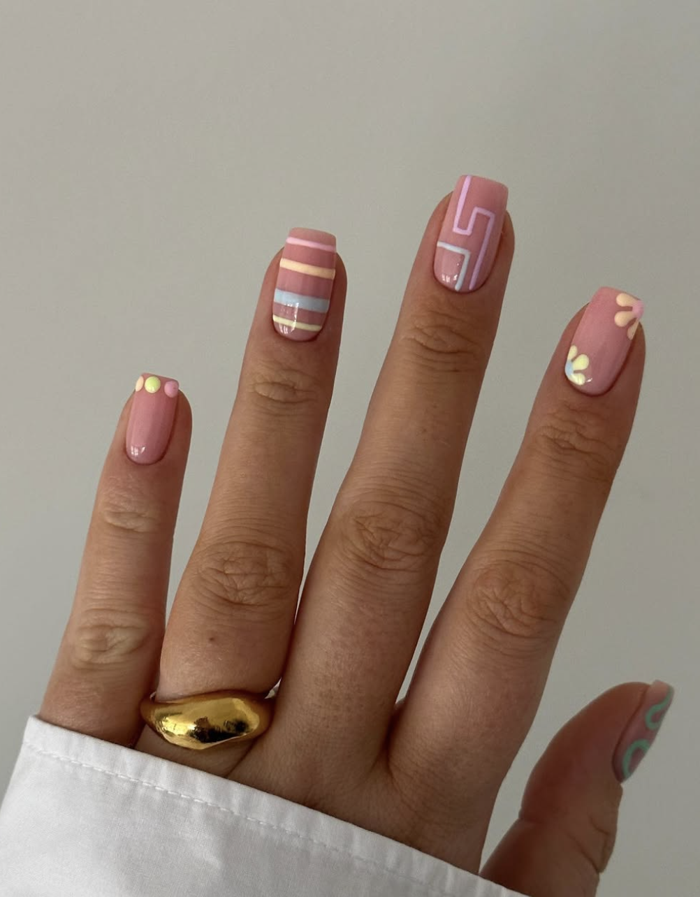 A close-up of short nails featuring a geometric color-block design with muted pastel shades of pink, blue, and sage green.