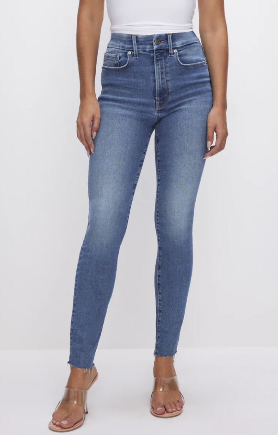 Model wearing Good American Always Fits Good Waist Skinny Jeans in a medium wash, featuring a gap-proof high waistband and reinforced stitching designed to fit muscular thighs on an athletic figure.