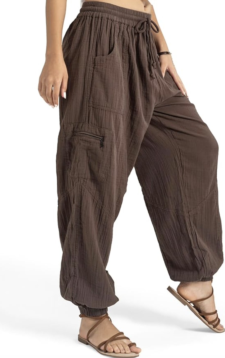A close-up of a person wearing dark brown, oversized cotton harem pants with a drawstring elastic waistband and a side cargo zipper pocket.