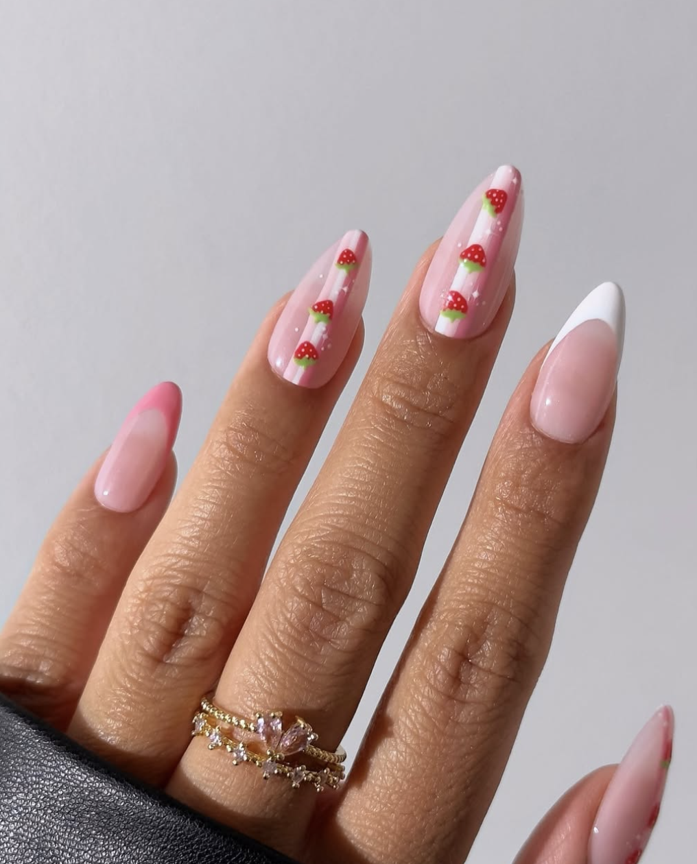 Long almond-shaped nails with a pink French tip base featuring hand-painted red strawberries with white seeds and green leaves.