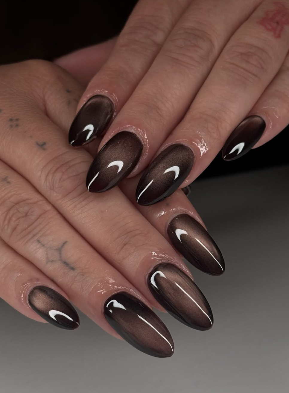 A close-up of almond-shaped nails featuring a dark chocolate-brown aura design with a glossy, airbrushed glow effect.