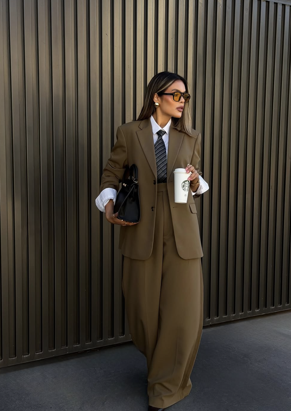 A woman wearing a tailored tan monochromatic blazer and matching wide-leg trousers, styled with a dark handbag for a polished, professional look.
