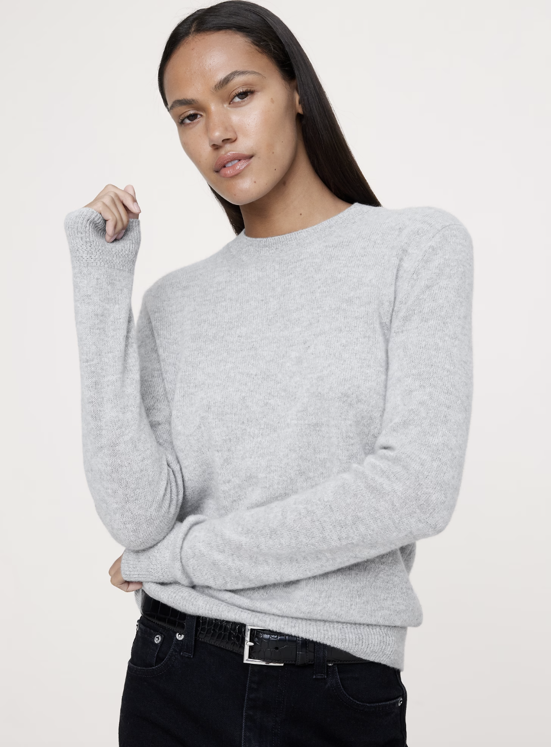 A woman wearing a grey lightweight cashmere crew-neck sweater, a professional staple for styling business casual outfits with sneakers.