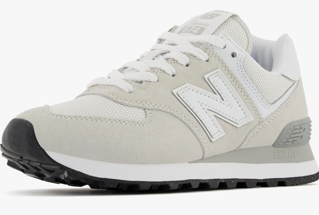 A product shot of the New Balance Women's 574 Core Sneaker in a neutral white and grey colorway. This shoe is recommended as a functional, urban finishing touch for the "Urban Drape" blazer outfit formula.