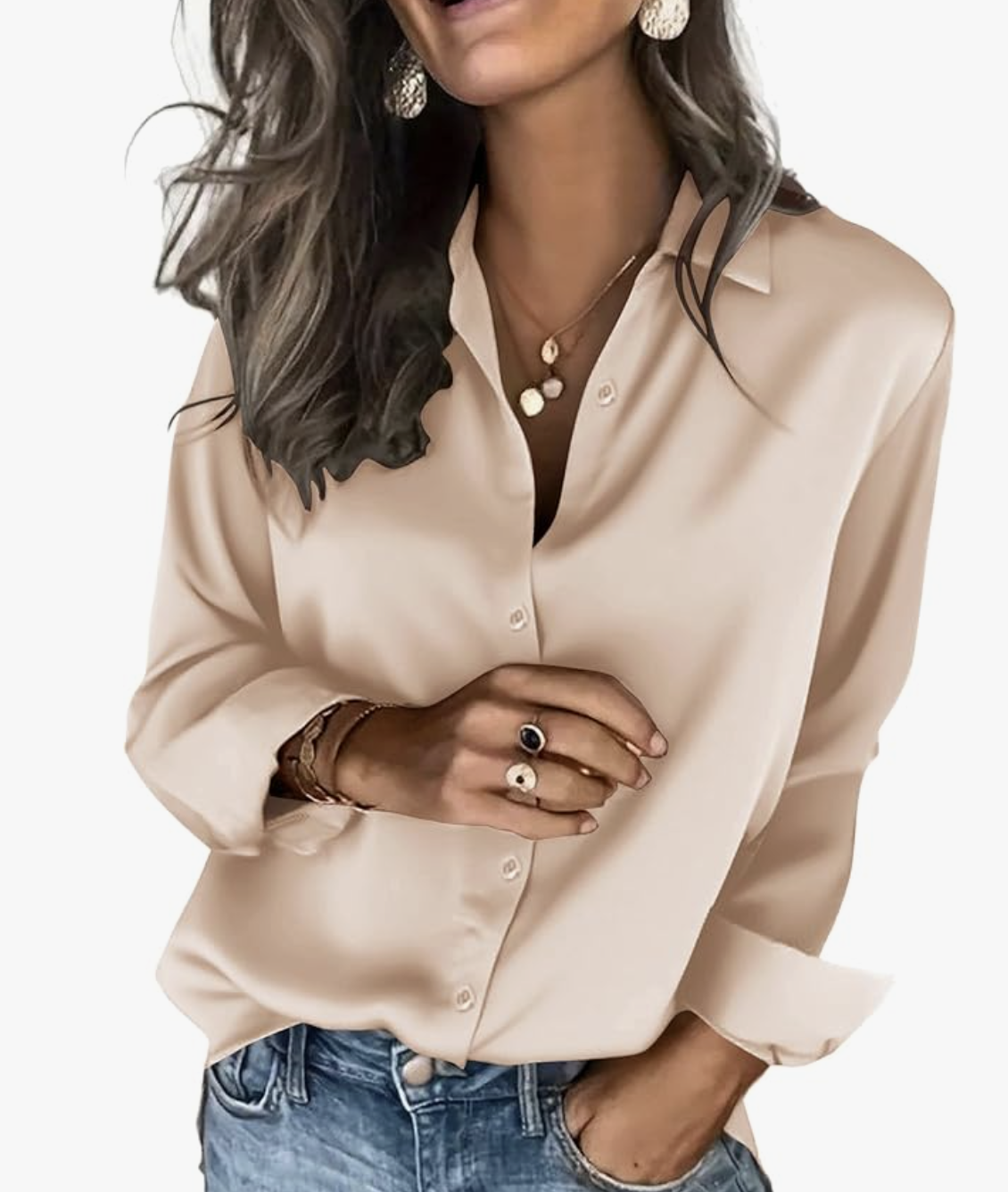 A woman wearing a champagne-colored satin button-down blouse tucked into blue jeans, accessorized with gold pendant necklaces and rings.