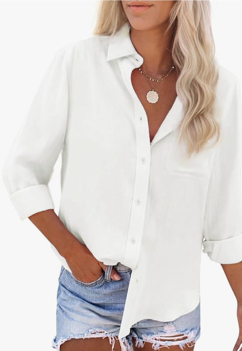 A woman wearing an oversized white cotton linen button-down shirt over denim shorts, demonstrating how to layer a shirt over a spaghetti strap dress.
