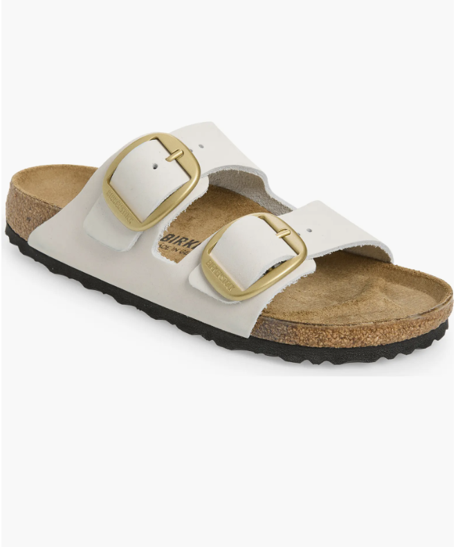 A close-up of off-white Birkenstock Arizona slide sandals featuring oversized gold buckles, a top capsule wardrobe pick.