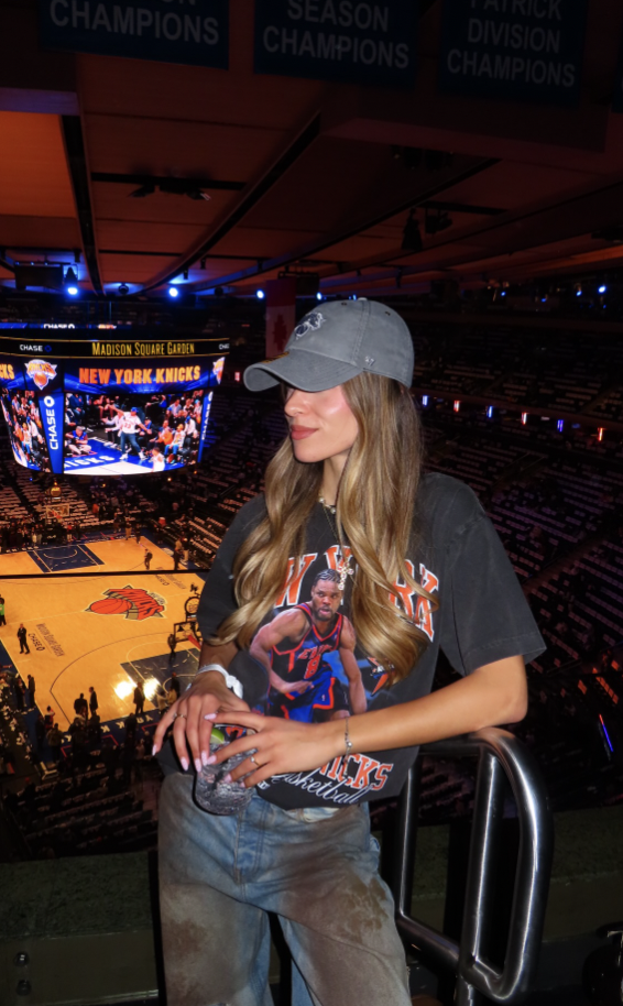 Woman at a basketball arena wearing an oversized team T-shirt, wide-leg jeans and a baseball cap.