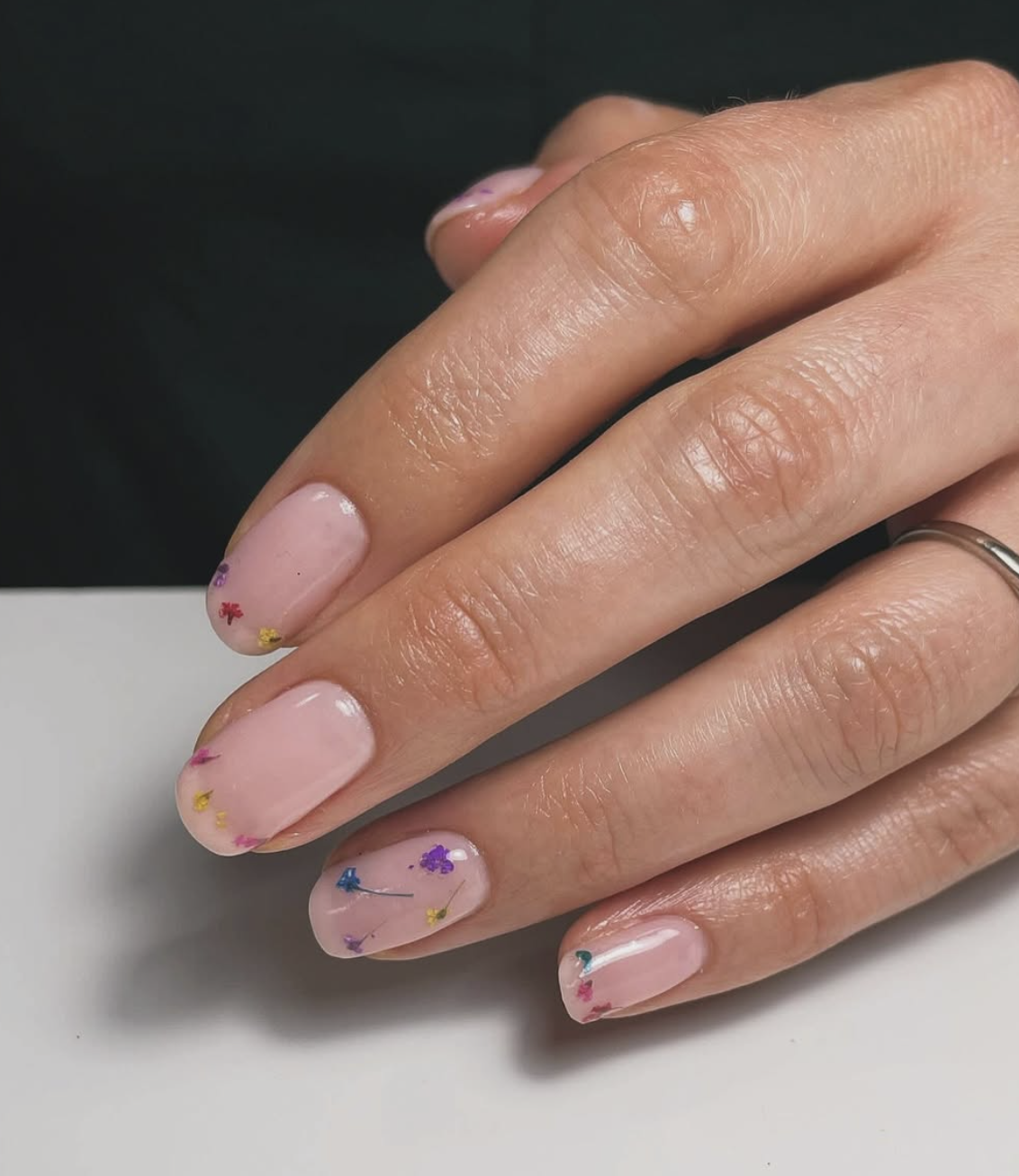 Long square-shaped gel nails with a sheer pink base and real colorful dried flowers encapsulated in clear gel.