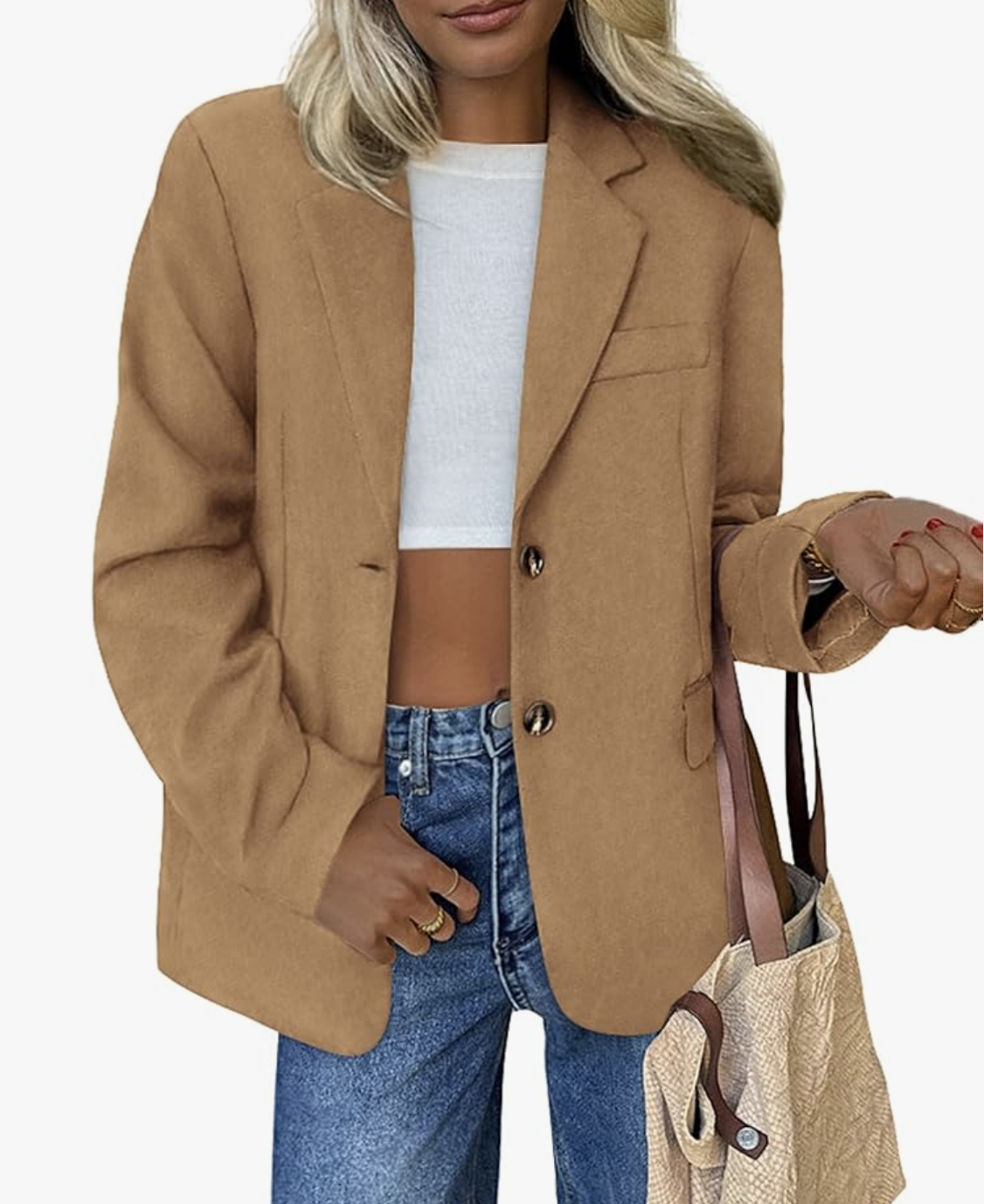 A woman wearing an oversized camel-colored blazer over a white crop top and blue jeans, showing a modern way to style structured outerwear for a casual look.