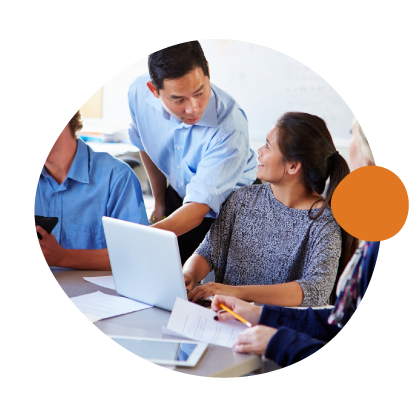 Group of people in a professional setting collaborating around a laptop and papers, with one person standing and two seated, during a meeting or discussion.