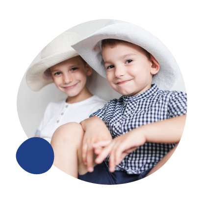 Two young boys wearing large white sun hats, smiling at the camera, sitting close together.