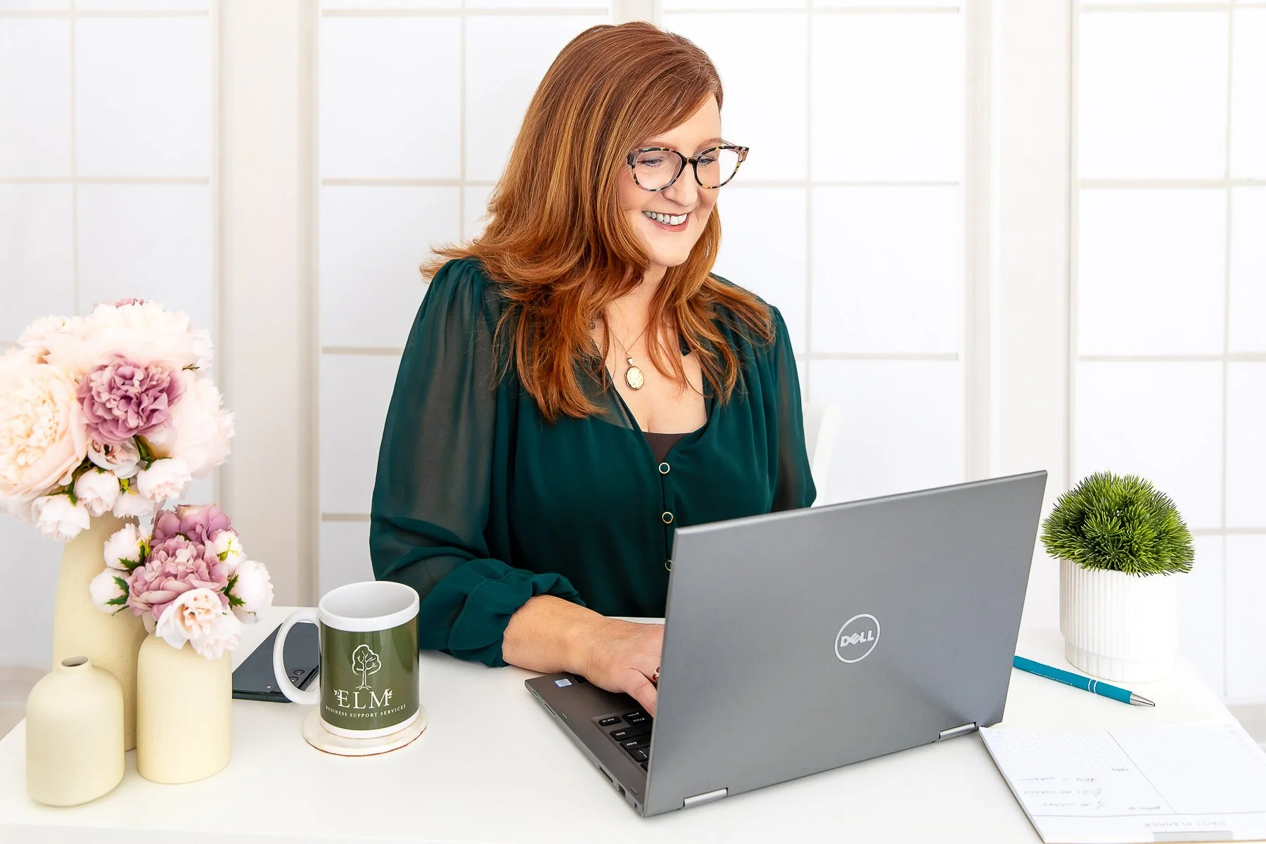 Woman typing on a computer with her ELM coffee mug beside her smiling during her branding photoshoot