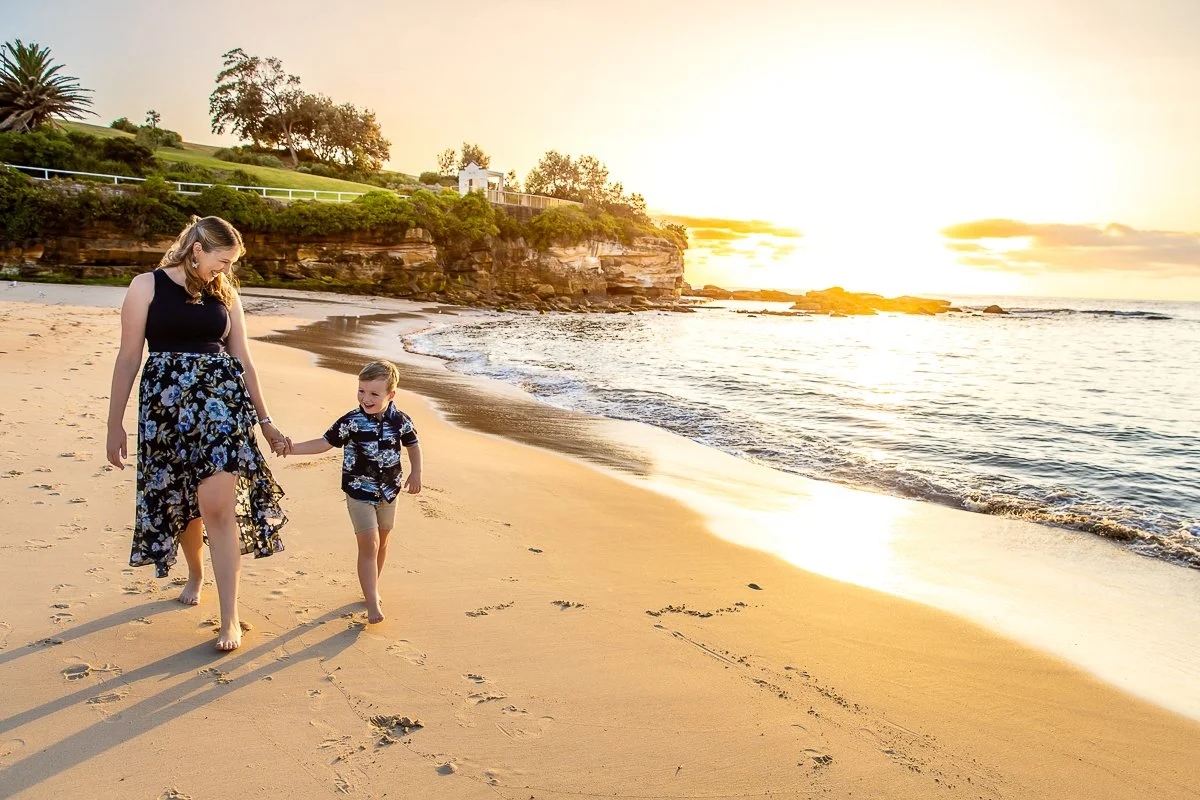 A mother and young son walking along Coogee Beach in the spectacular sunrise light
