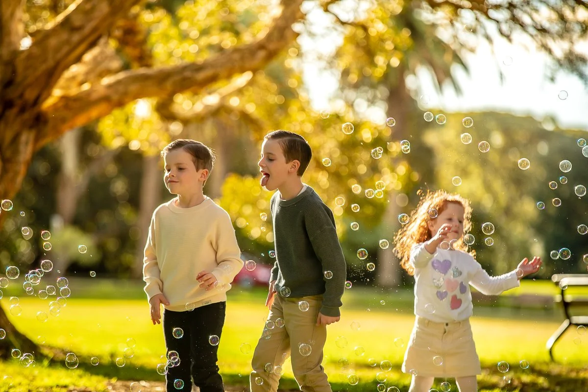 A family chasing bubbles in the afternoon sun at Centennial Park in Sydney's eastern suburbs for a family photoshoot