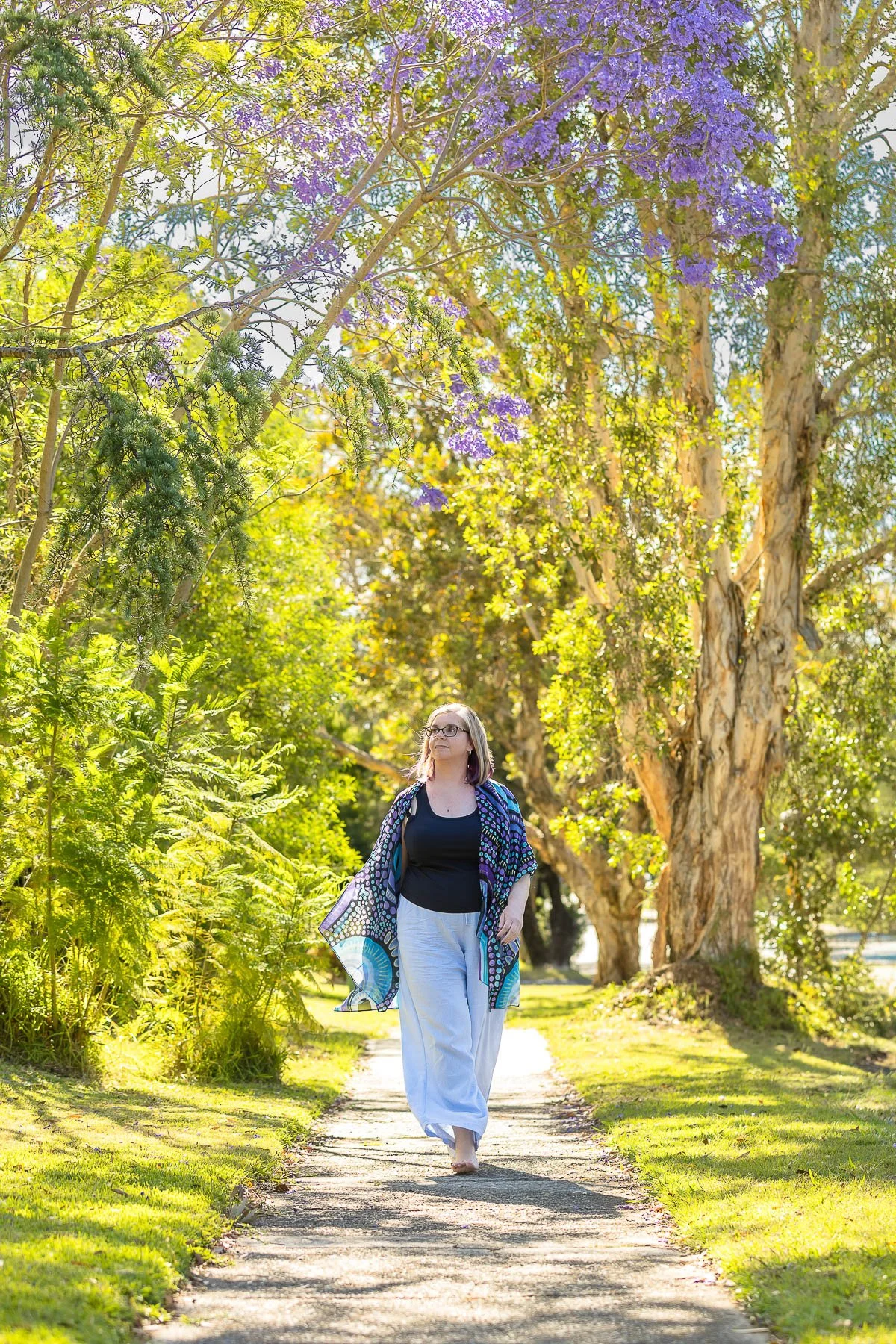 A woman walking barefoot down the path with jacaranda in the background during her branding photoshoot in the hills district
