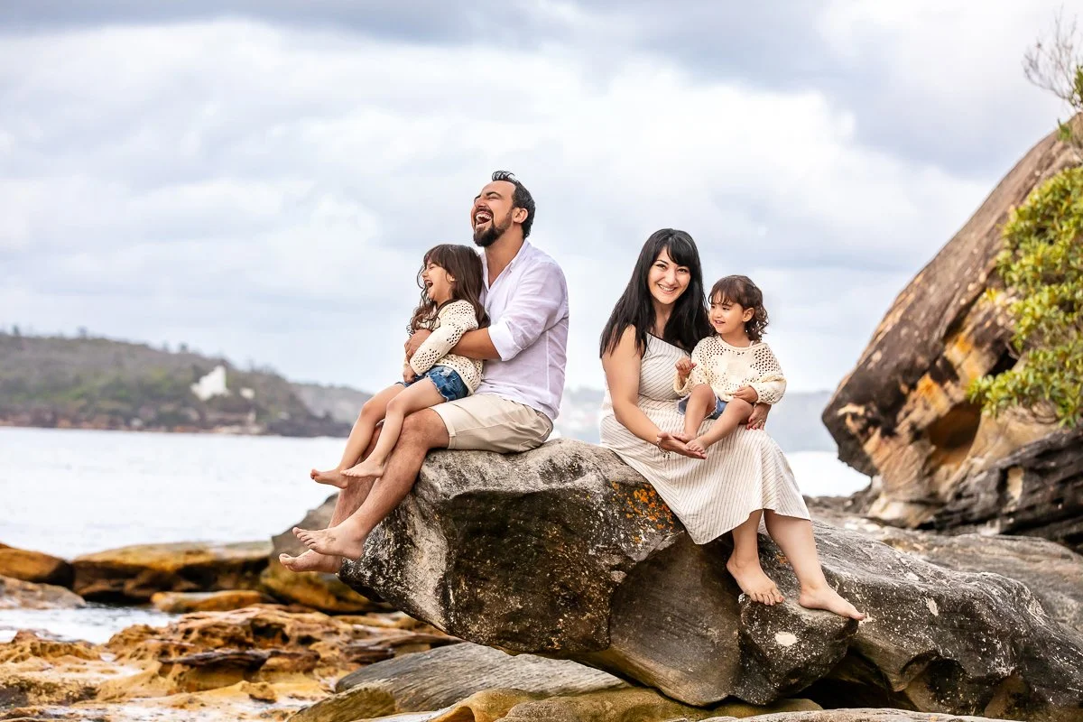 A young family sitting on the rocks and laughing and hugging during a family photoshoot at Balmoral Beach