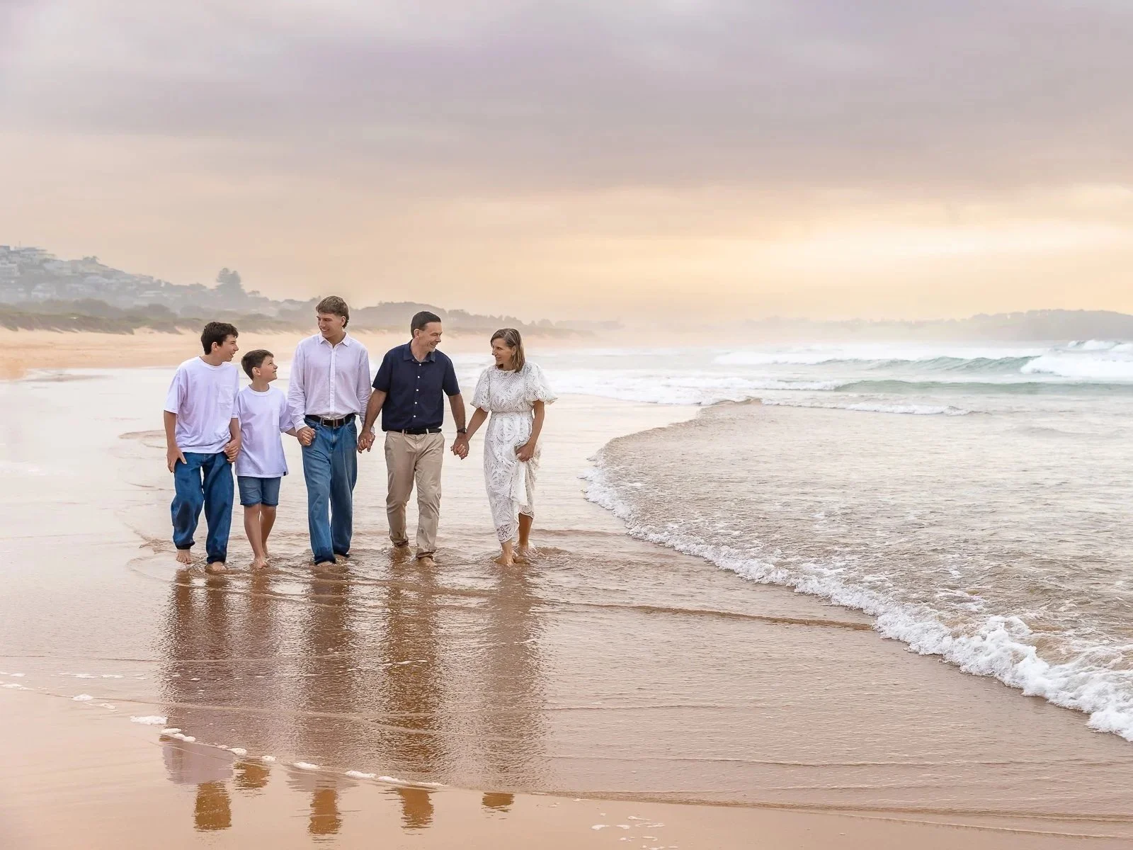 Family with 3 teenage boys walking hand in hand along Dee Why beach Sydney during a sunrise family photoshoot