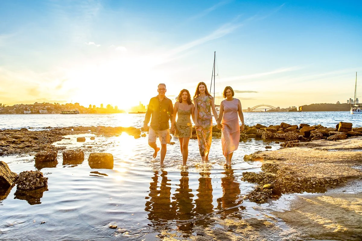 A family with teenagers walking in water at Milk Beach near Strickland House in Vaucluse in Sydney's Eastern Suburbs during a sunset family photoshoot with the Sydney city, Harbour Bridge and Opera House in the background
